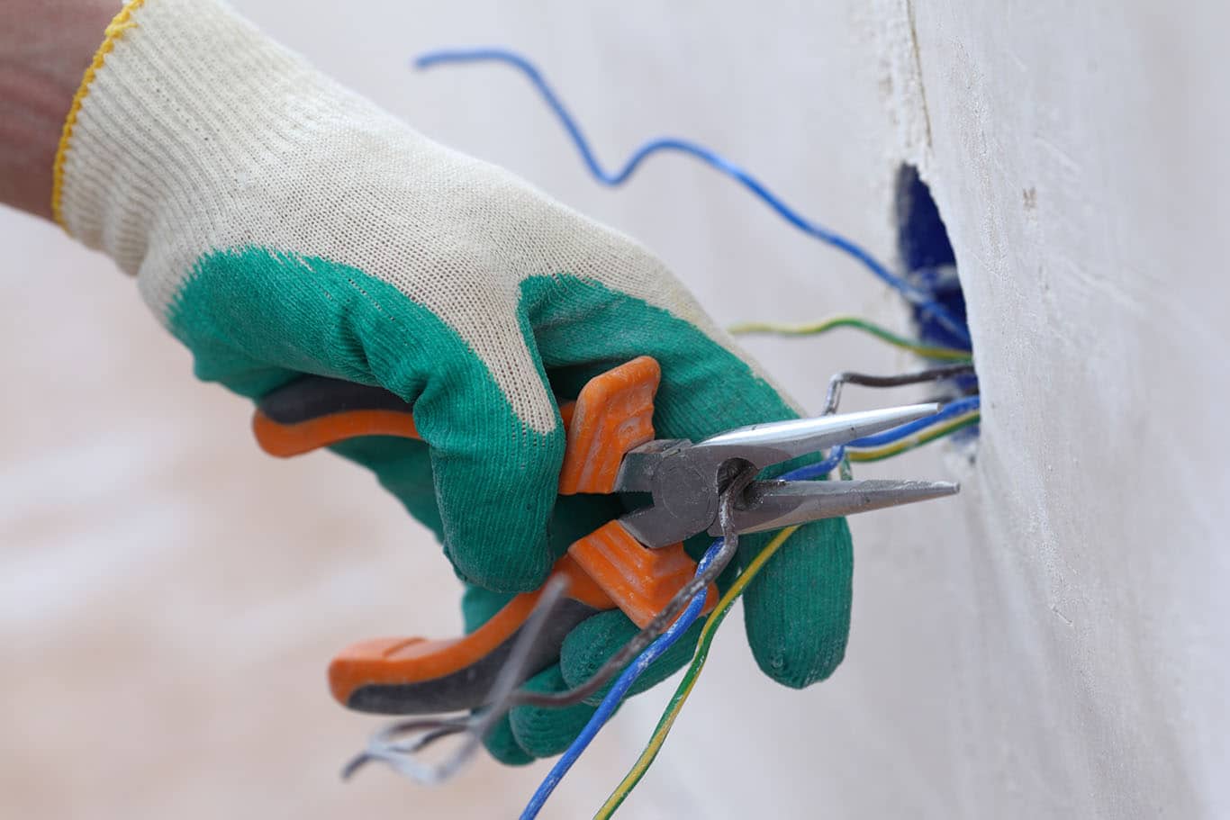 Gloved hands working on electrical wires with a hand tool